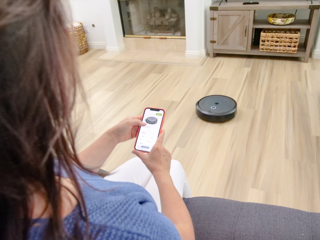 Una mujer que controla un robot aspirador usando una aplicación de teléfono inteligente sobre un piso de madera.